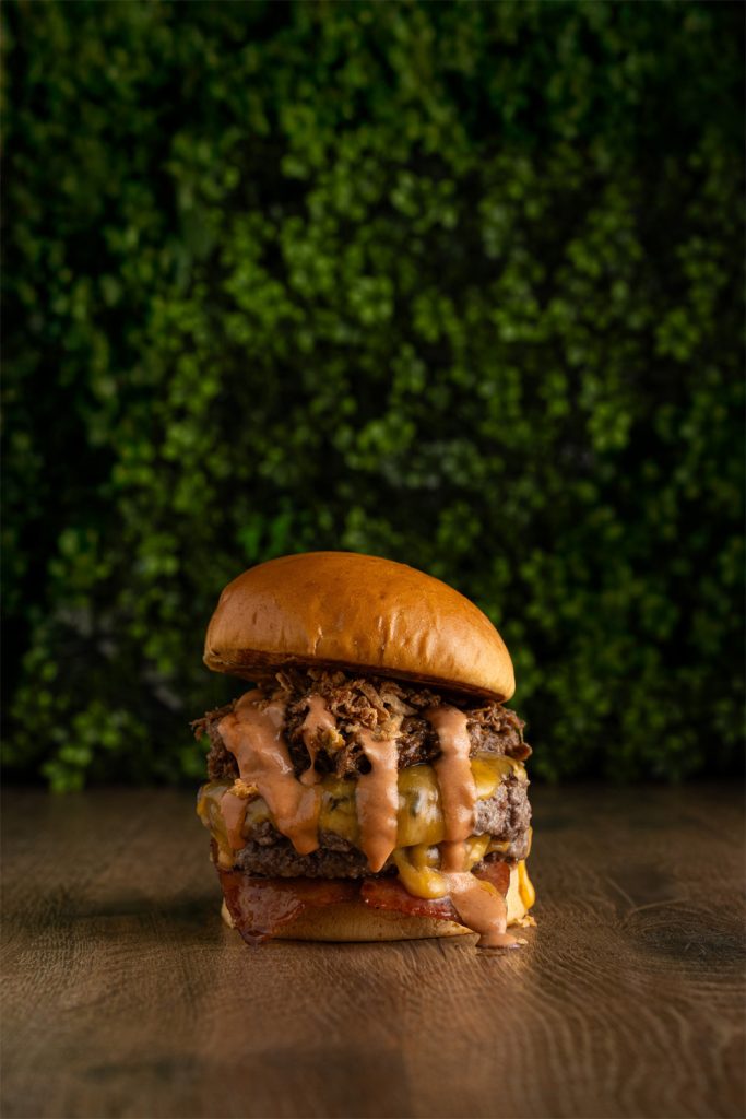 Fotografía profesional de hamburguesa con queso fundido y salsa chorreando, realizada por fotógrafo de hamburgueserías en Sevilla