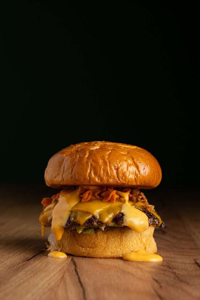 Hamburguesa con queso cheddar fundido chorreando fotografiada por fotógrafo profesional para hamburgueserías en Sevilla