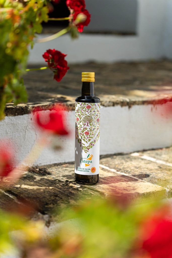Fotografía de botella de aceite de oliva virgen extra Estepa en escalones de cortijo andaluz con flores rojas