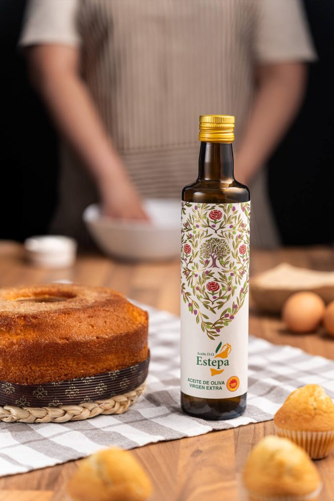 Fotografía de botella de aceite de oliva virgen extra Estepa junto a bizcocho y muffins en escena de repostería