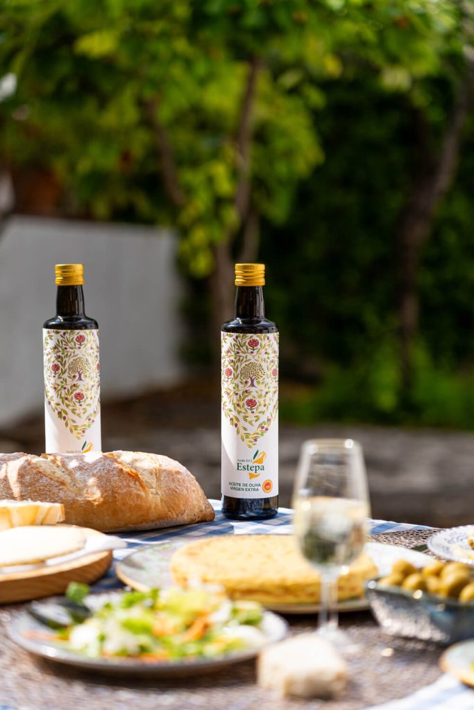 otografía de botellas de aceite de oliva virgen extra Estepa en mesa exterior con pan y tortilla, fotógrafo Sevilla