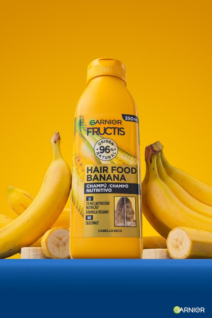 Fotografía de producto champú Garnier Fructis Hair Food Banana rodeado de plátanos sobre fondo amarillo en estudio Sevilla