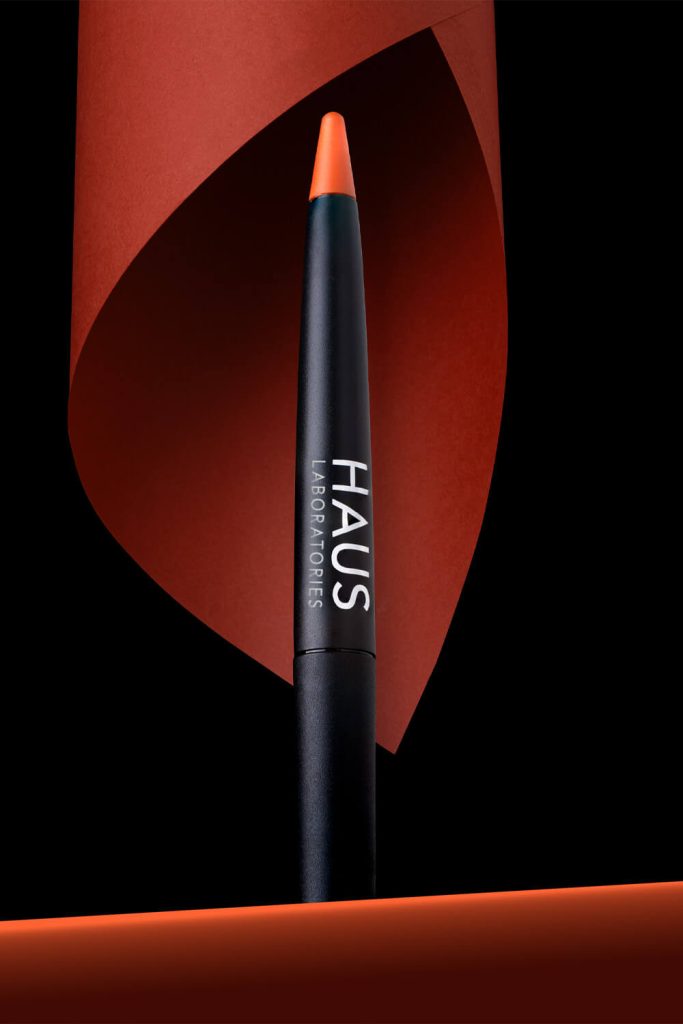 Fotografía de producto lápiz de labios Haus Laboratories naranja con composición de papel rojo en estudio Sevilla
