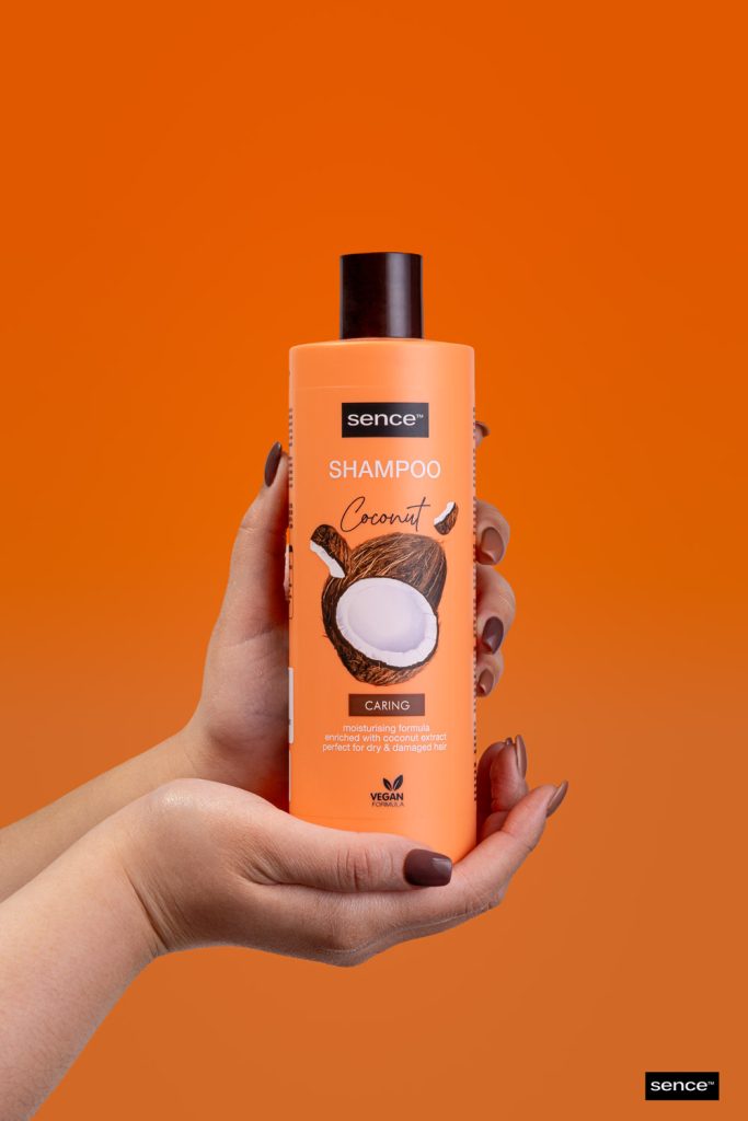 Fotografía de producto champú Sence Coconut sostenido por manos sobre fondo naranja en estudio Sevilla