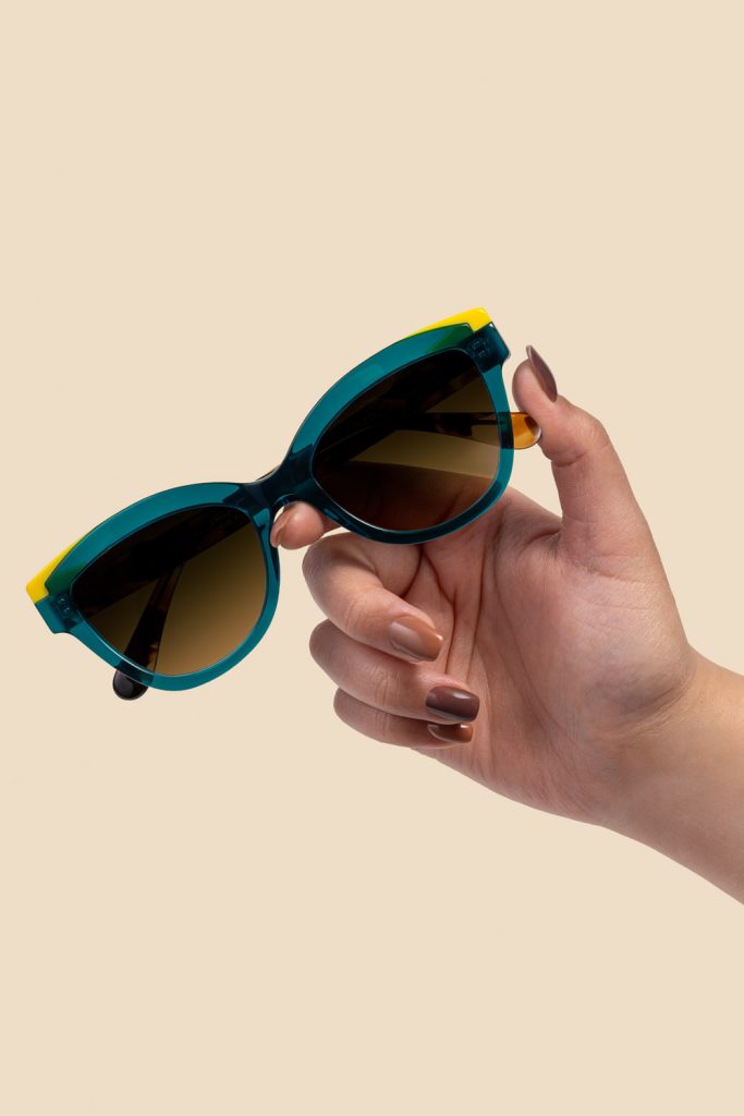 Fotografía de producto gafas de sol bicolor sostenidas por una mano sobre fondo neutro en estudio Sevilla